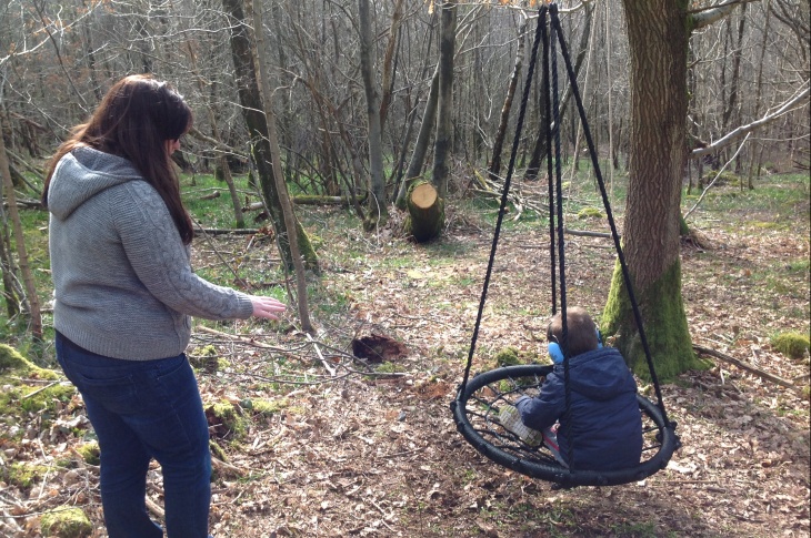 A mother and child playing on a woodland swing